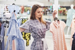 This dress is perfect. Young beautiful smiling woman makes choice when shopping at a store.