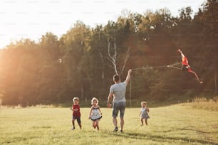 pai de família feliz e filhos correm com uma pipa no prado.