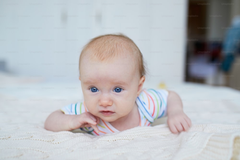 Adorable niña acostada en la cama boca abajo. Feliz y saludable niño pequeño practica el gateo. Niño pequeño en guardería soleada haciendo tiempo boca abajo