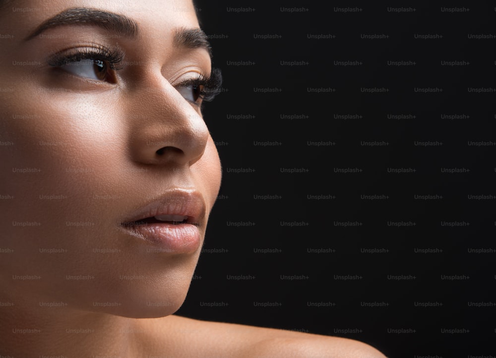 Close up of woman appearance with long eyelashes looking aside. Copy space in right side. Isolated on black background