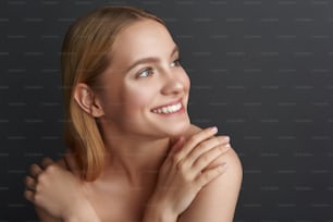 Close up of positive young woman expressing happiness and looking into the distance with a smile while being isolated against the grey background