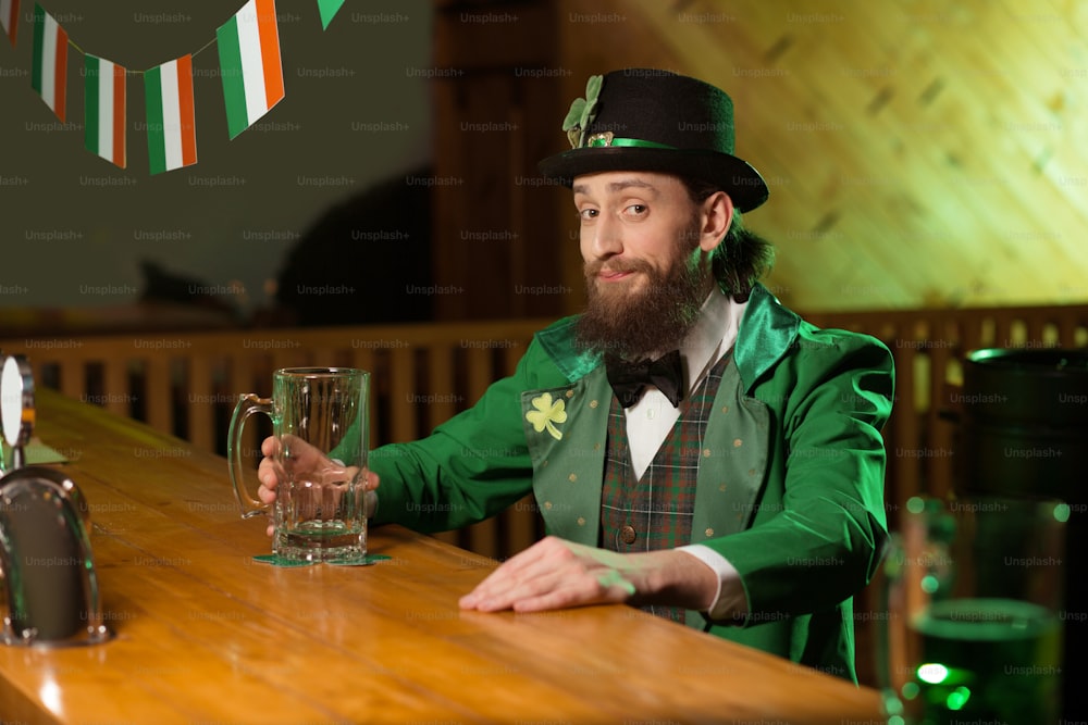 Lots of beer. Dark-haired bearded young man wearing a leprechaun costume looking merry