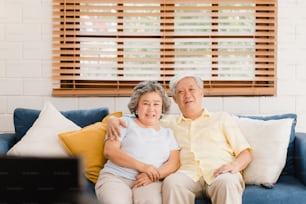 Asian elderly couple watching television in living room at home, sweet couple enjoy love moment while lying on the sofa when relaxed at home. Enjoying time lifestyle senior family at home concept.