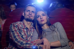 映画館で一緒に座って、コメディやロマンチックな映画を見ているカップルの正面図。ハンサムなひげを生やした男は、映画のレビュー中に近くに座っている美しいガールフレンドを抱きしめています。レジャーのコンセプト。