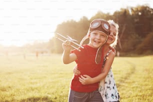Brother and sister are playing together. Two children playing with a wooden airplane outdoor.