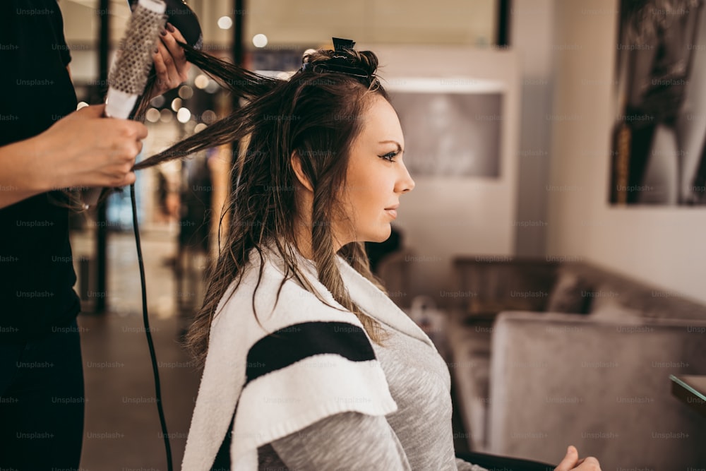 Beautiful brunette woman with long hair at the beauty salon getting a hair blowing. Hair salon styling concept.