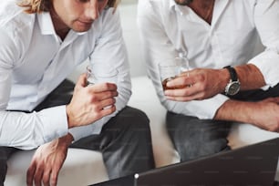 À la recherche de l’étoffe. Vue particulaire des deux hommes d’affaires assis près de l’ordinateur portable et tenant un verre de whisky.
