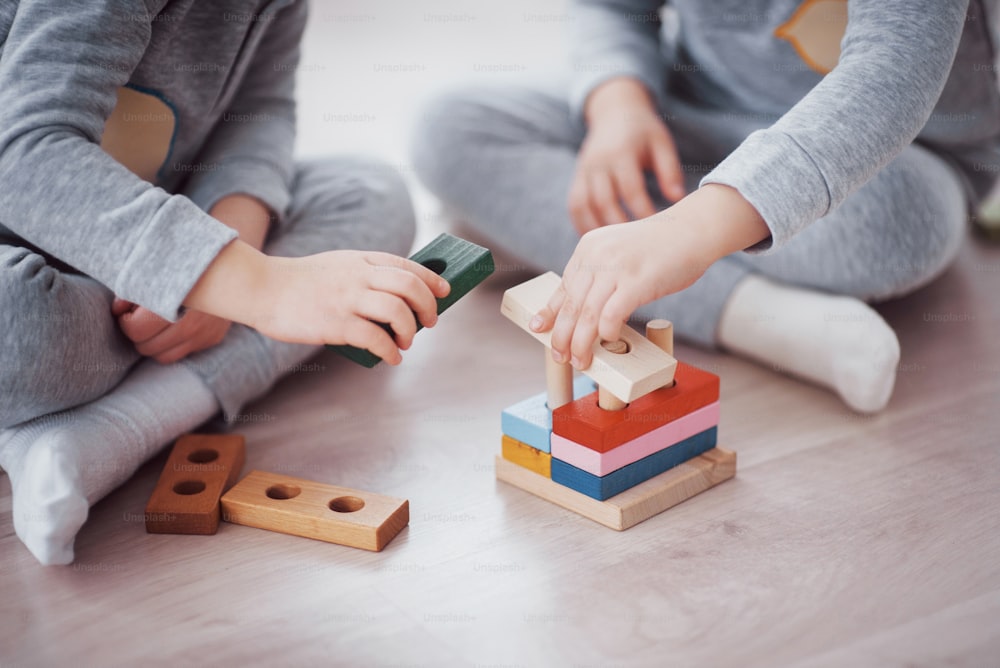 Los niños juegan con un diseñador de juguetes en el suelo de la habitación infantil. Dos niños jugando con bloques de colores. Juegos educativos de jardín de infantes. Vista de cerca.