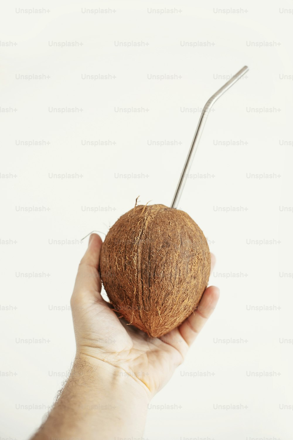 Hand holding coconut with metal straw on white background. Hello summer vacation concept. Zero waste, sustainable lifestyle on tropical island. Copy space. Ban plastic, ecological problem