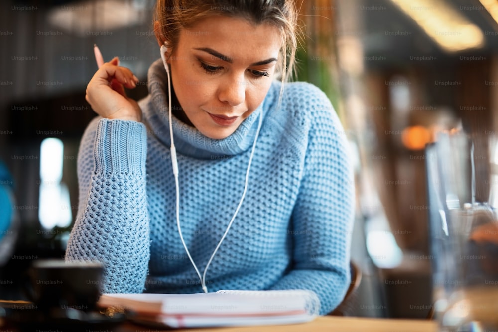 Young female freelancer going through weekly planner while listening music on coffee break in cafeteria.