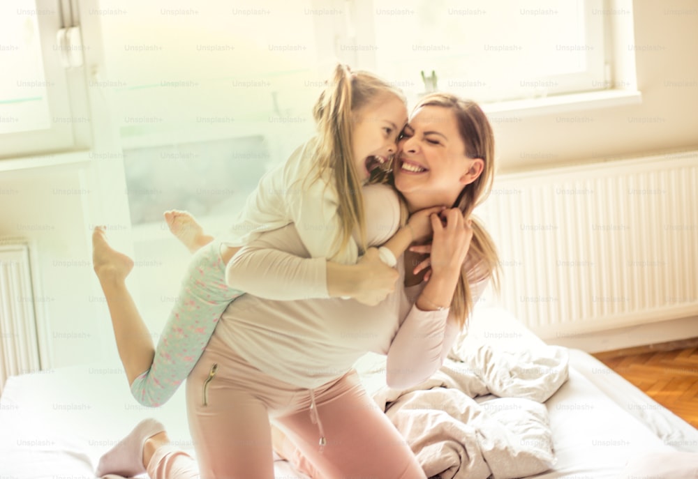 Strongest connection. Mother and daughter have piggyback ride in bed.