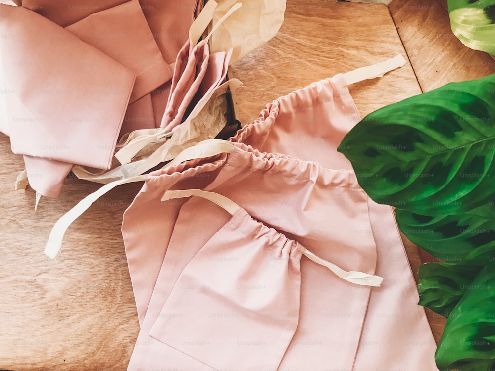 Eco friendly reusable bags on wooden background with green leaves plant, flat lay. Zero waste shopping concept. Ban single use plastic. Eco bags for groceries. Sustainable lifestyle