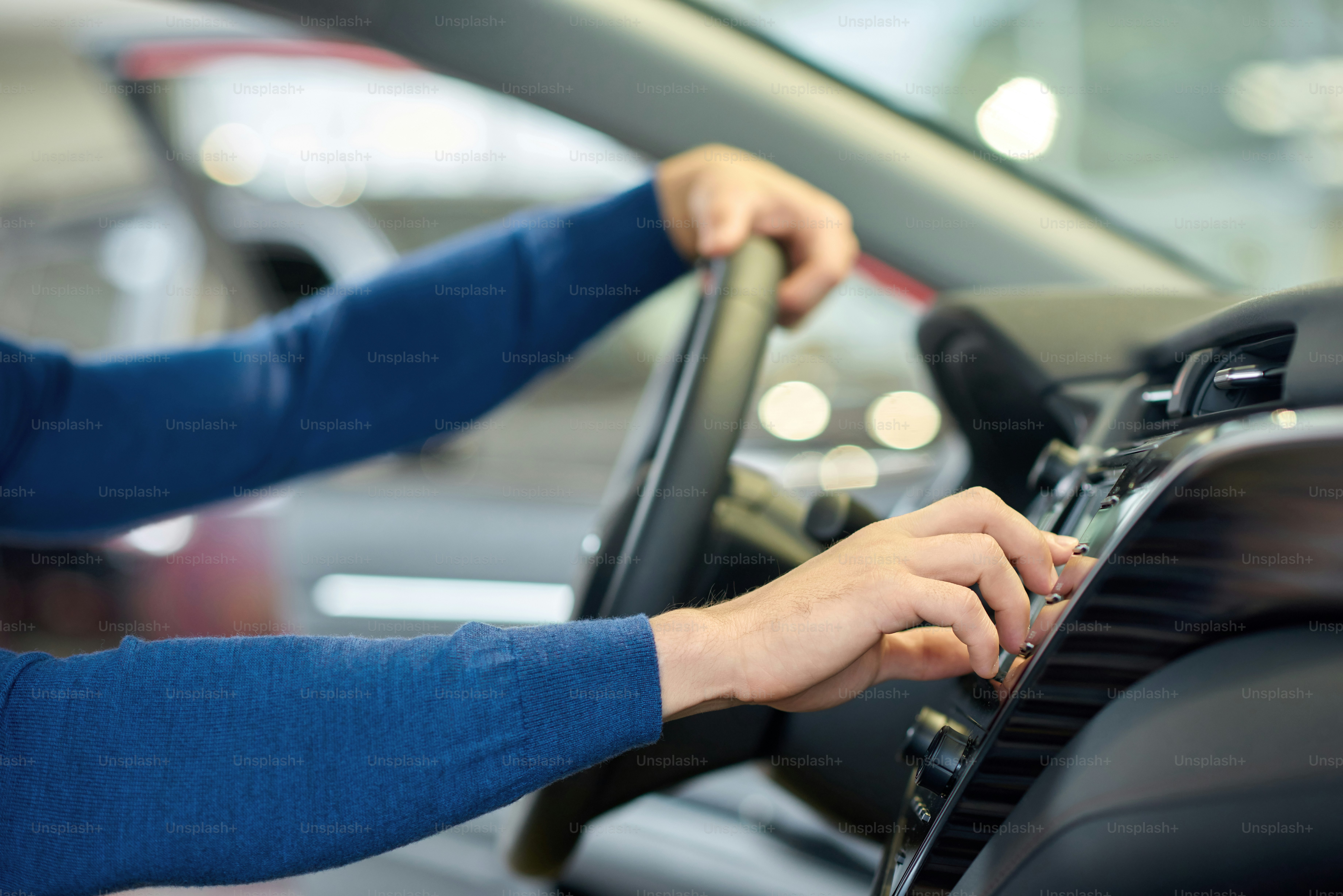 Close up of man's hands in blue sweater. Driver sitting in car and holding on his hand on steering wheel and turning on heating. Crop of well-groomed male arms when guy choosing music in auto.