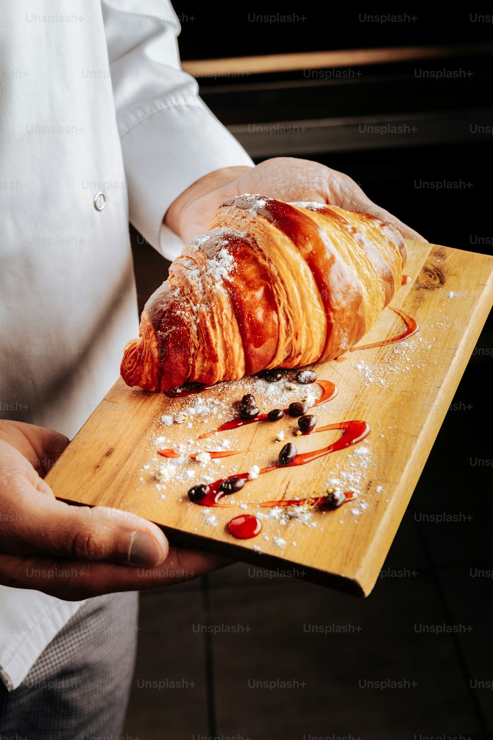 With sugar powder. Talented young baker holding wooden plate with croissant with sugar powder