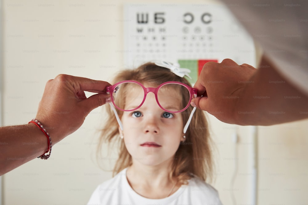 背景の視力を確認するためのボードでピンクの眼鏡を見ている子供。