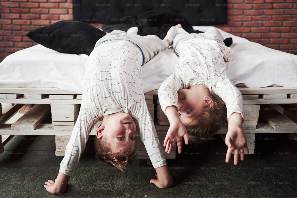 Happy kids playing in black bedroom. Little boy and girl, brother and sister play on the bed wearing pajamas.