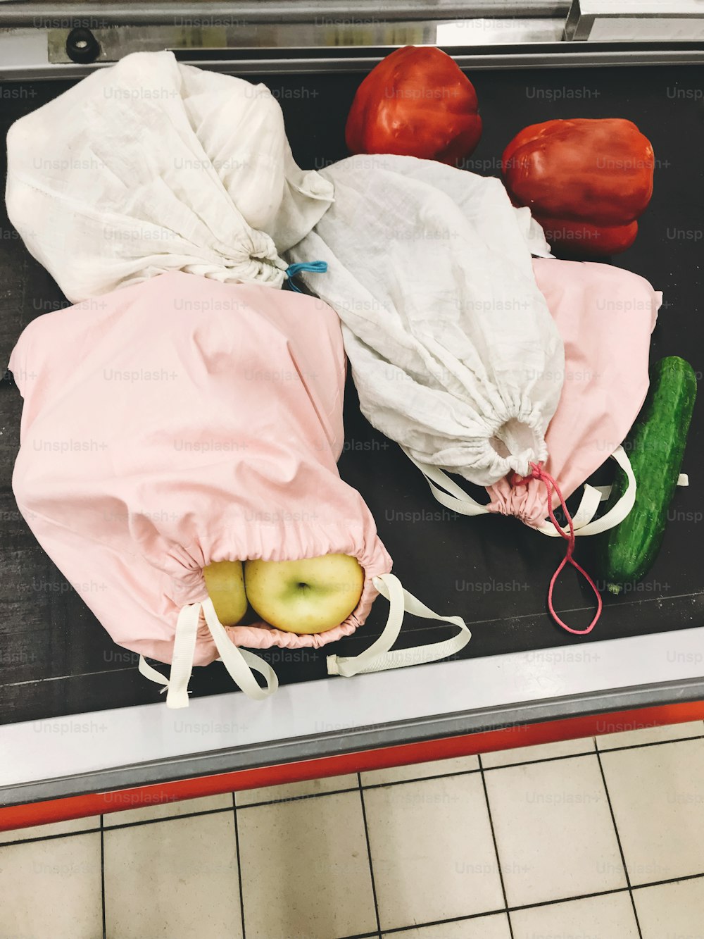 スーパーマーケットのレジカウンターの列に並ぶ野菜や果物の入ったエコ再利用可能なバッグ。ゼロウェイストショッピングのコンセプト。使い捨てプラスチックの禁止。食品用のエコリネンバッグ。サステナブルなライフスタイル