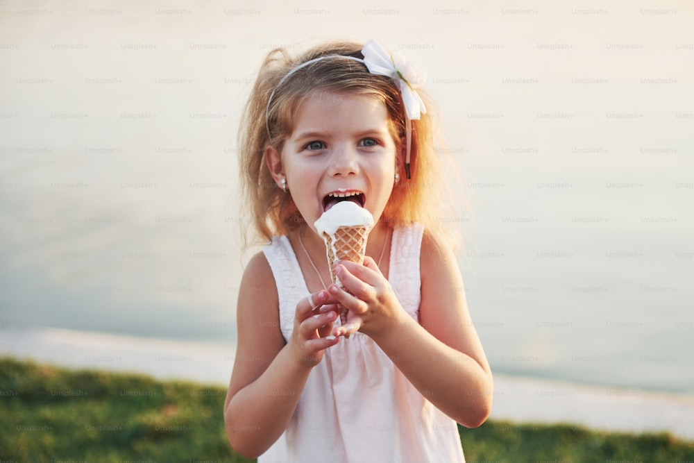 A beautiful little girl eats an ice cream near the water.