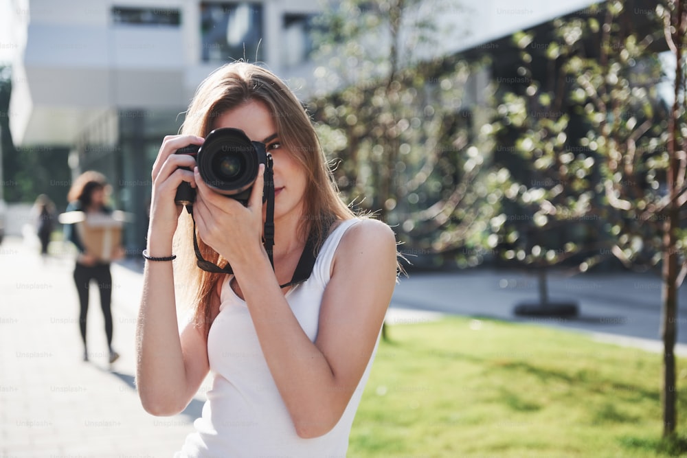 Une jeune photographe blogueuse tient à la main un appareil photo professionnel en plein air dans la ville.