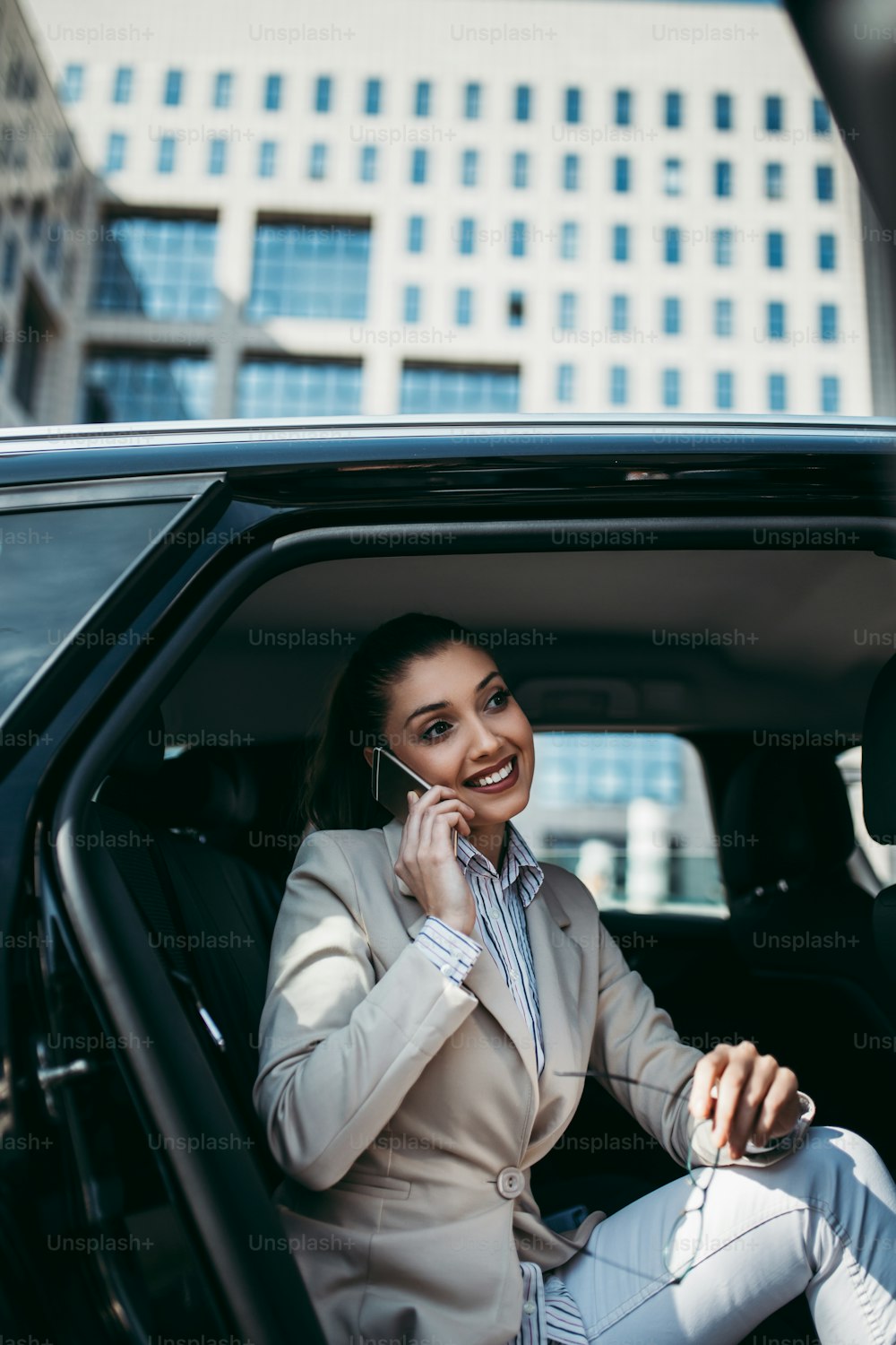 고급 자동차의 뒷좌석에 앉아 있는 잘 생긴 젊은 비즈니스 여성. 그녀는 스마트 폰을 사용하여 웃으며 밖을 내다 보았다. 기업 비즈니스 개념의 교통.