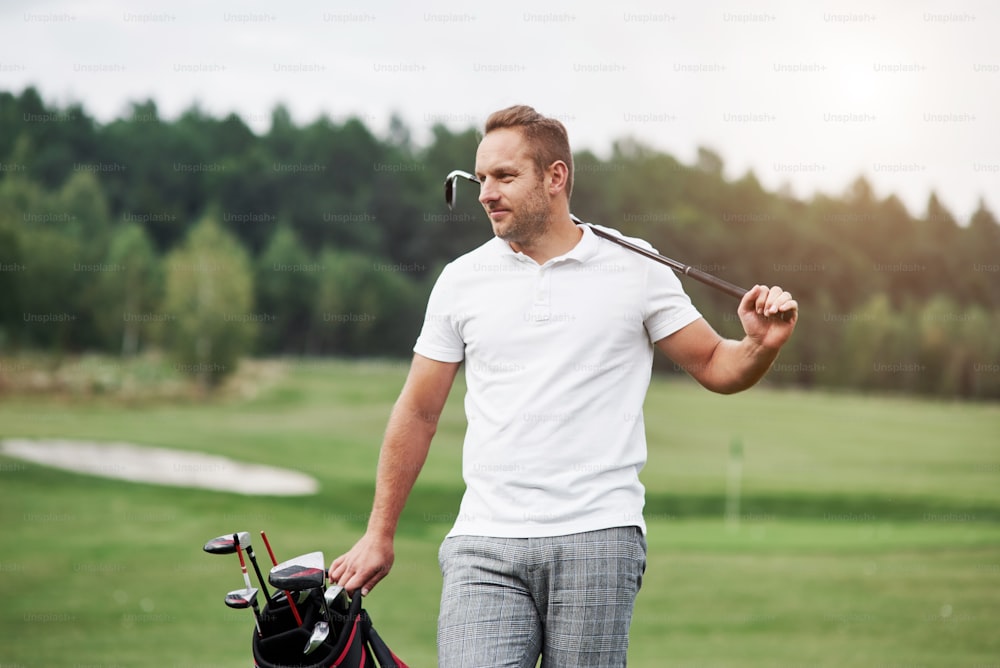 Ritratto di giocatore di golf a piedi nel prato e attrezzatura in mano. Boschi sullo sfondo.