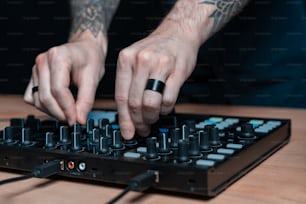 검은 어두운 벽 인테리어가 있는 집 방 스튜디오 내부의 전문 DJ 남자 창의적인 음악의 클로즈업 및 자른 사진 문신 손. 그는 공간 컨트롤러 기기를 사용합니다.