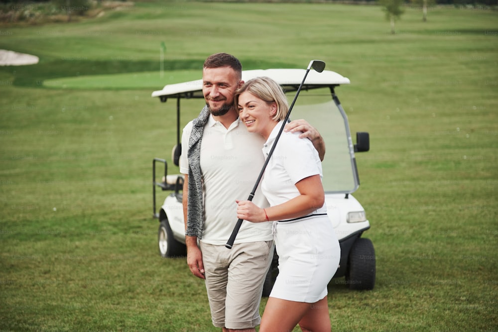 Two professional golfers, a woman and a man go together to the next hole. Lovers hug and smile, they have a date.