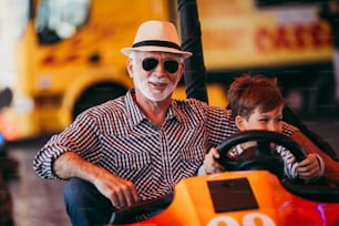 Grandfather and grandson having fun and spending good quality time together in amusement park. They enjoying and smiling while driving bumper car together.