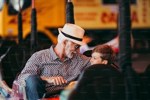 Grandfather and grandson having fun and spending good quality time together in amusement park. They enjoying and smiling while driving bumper car together.