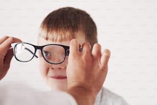 Smiling and looking at the woman. Doctor giving the child new black glasses for his vision.