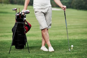 Porträt eines wandernden Golfspielers im Rasen und Ausrüstung in den Händen. Wald im Hintergrund.