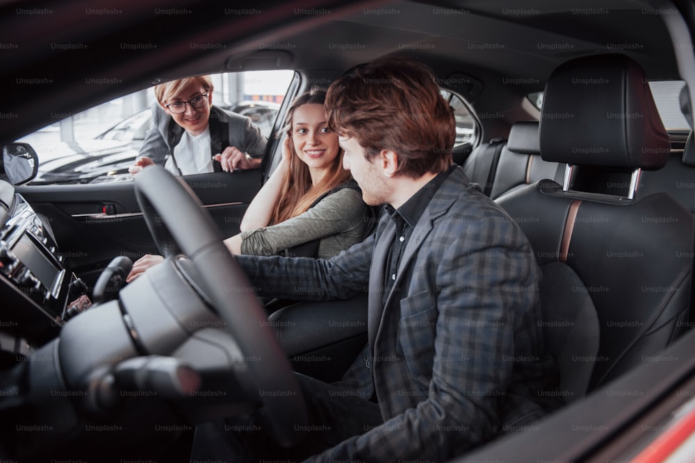 Happy beautiful couple is choosing a new car at dealership.