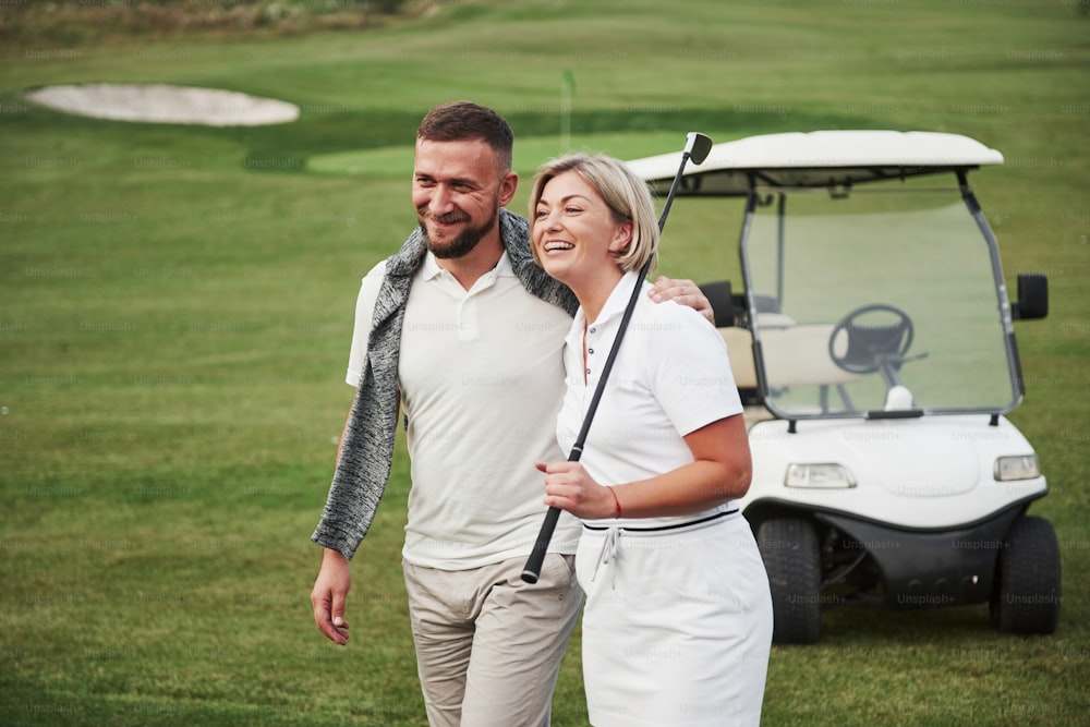 Deux golfeurs, une femme et un homme, se rendent ensemble au trou suivant. Une élève y va avec son entraîneur personnel et est satisfaite de son succès sportif.