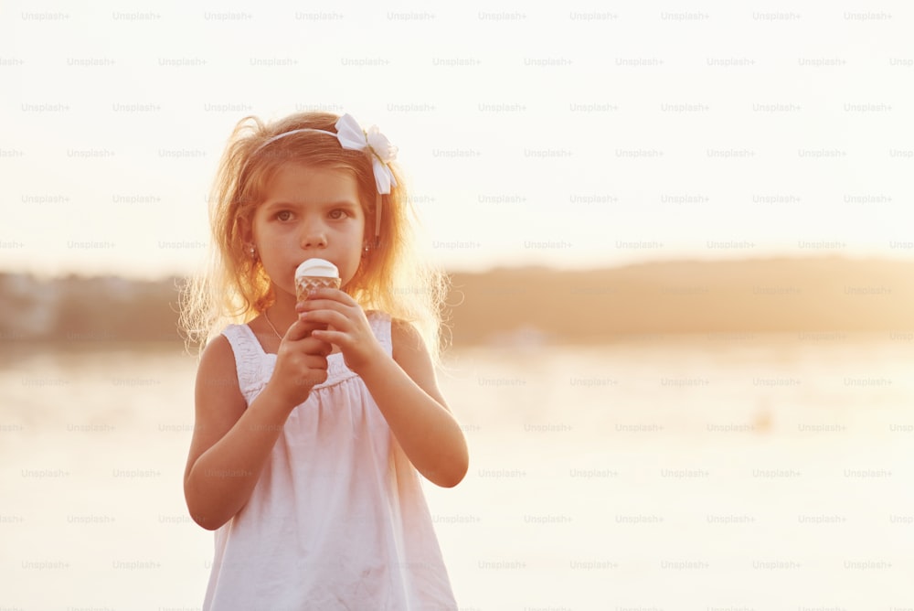 Cute little girl eating ice cream at background of lake and woods.