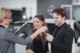 Buying their first car together. High angle view of young car salesman standing at the dealership telling about the features of the car to the customers.