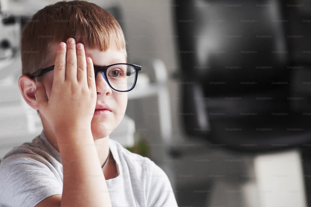 Front view. Close right eye with your hand. Little boy checking his vision with new black glasses.