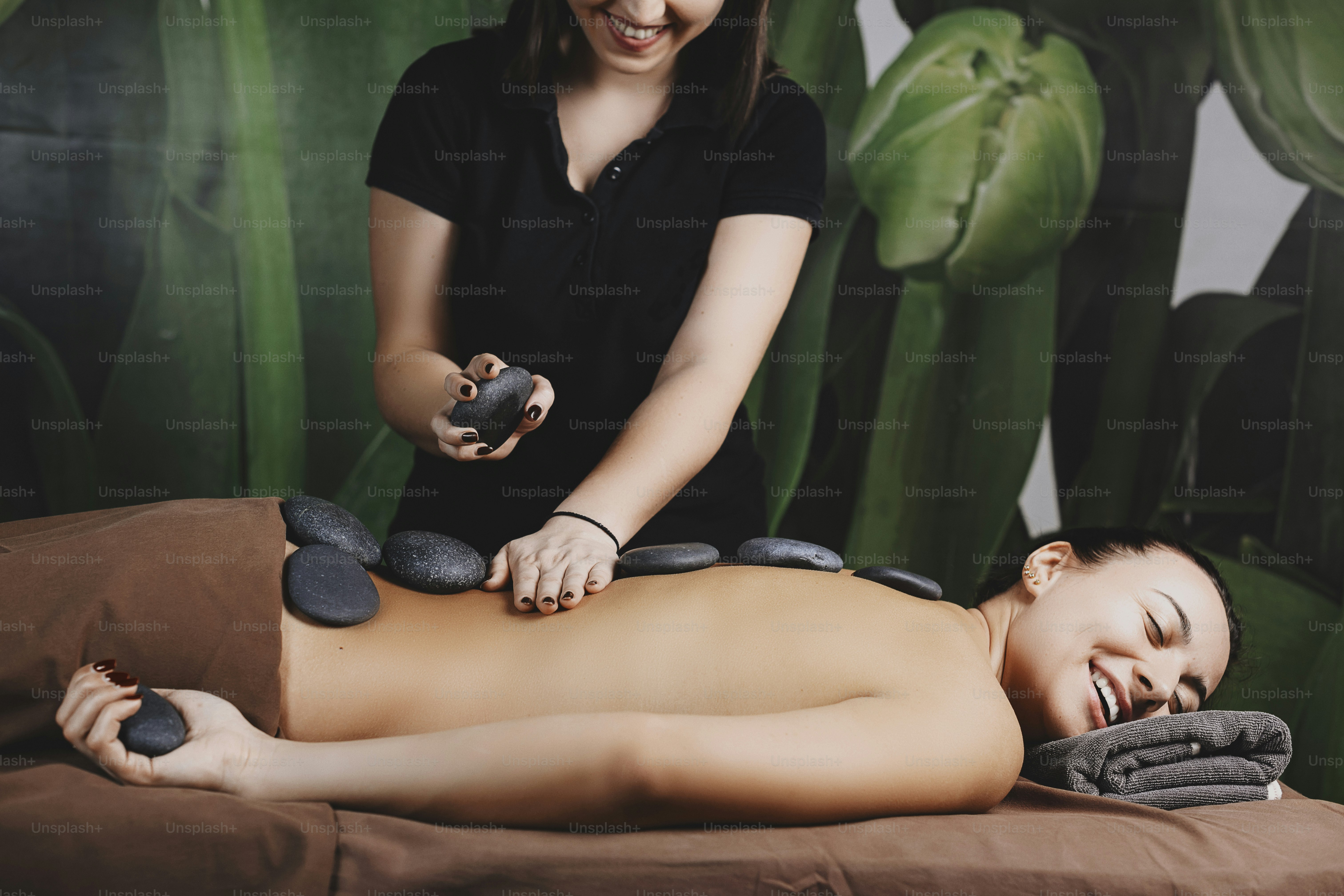 Tampilan samping seorang berambut cokelat Kaukasia cantik yang menjalani prosedur batu panas di punggungnya oleh pusat kesehatan spesialis spa.