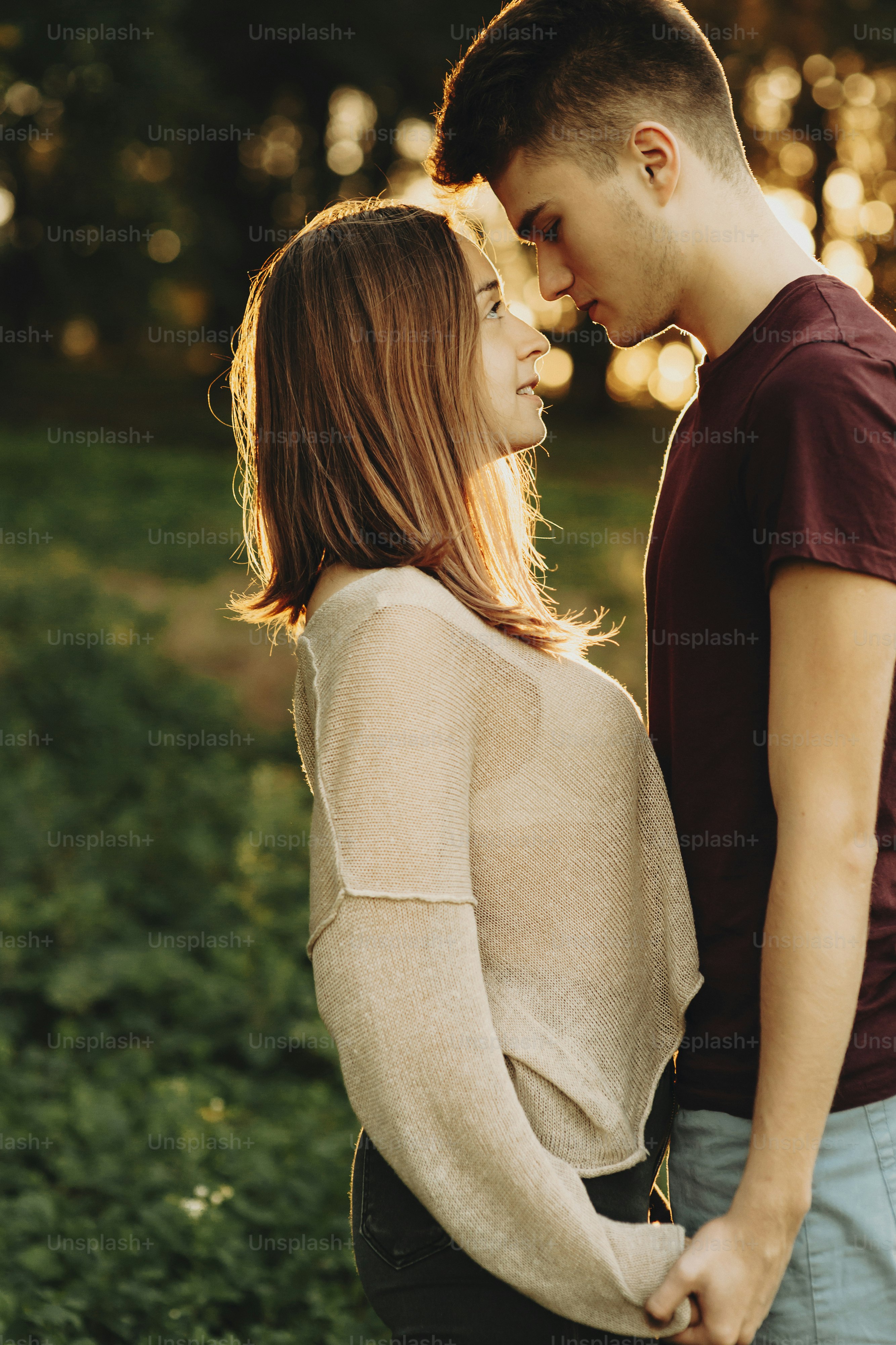 Side view portrait of a attractive young caucasian couple holding hands and looking one to another while girl is smiling and man is looking seriously against sunset while dating.