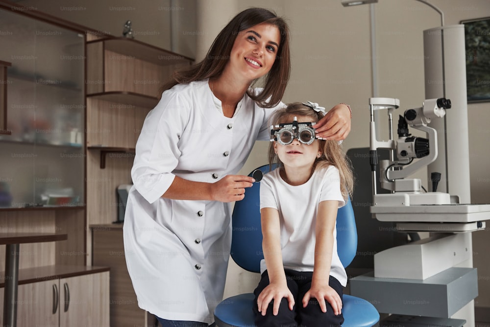 Medizinprodukt im Hintergrund. Kleines Mädchen mit Brille, das in der Klinik sitzt und ihre Augen testen lässt.