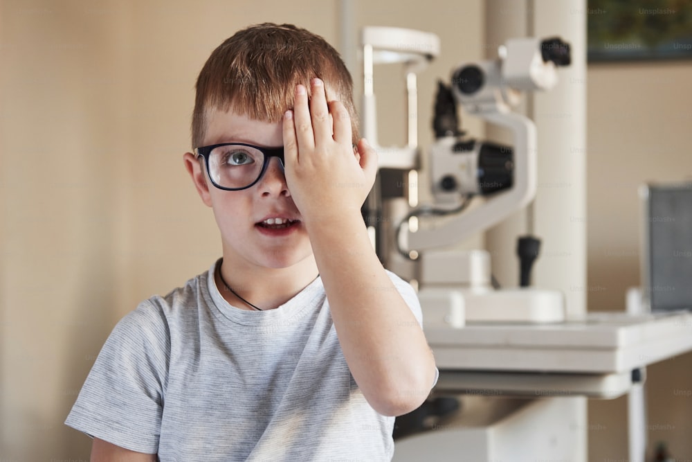 Petit garçon couvrant son œil et ayant une vue d’examen à la clinique.