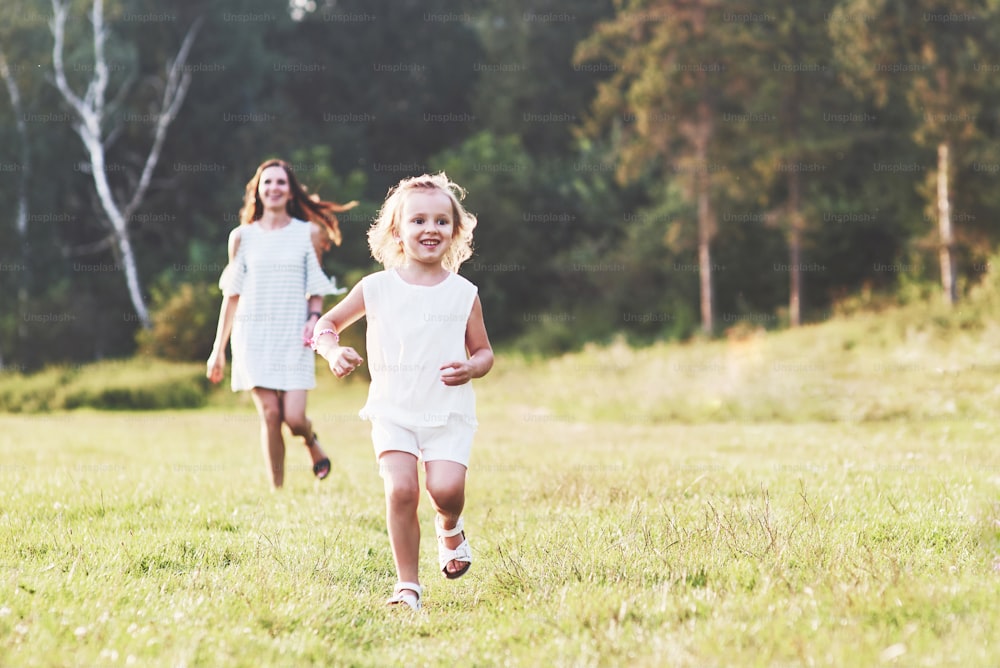 Mom and little girl have walk outside on the field and woods at background.