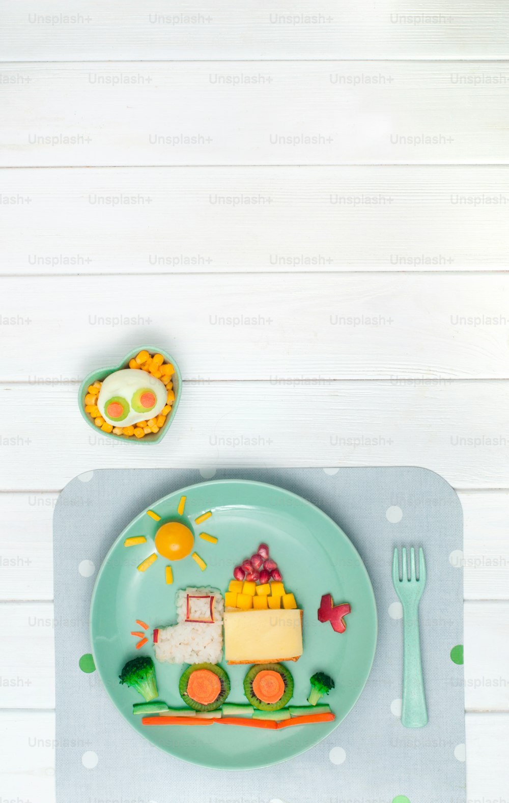 Kids food art concept: car from rice, sandwich and fresh fruits and vegetables on the plate with napkin on white wooden background with blank space for text; top view, flat lay