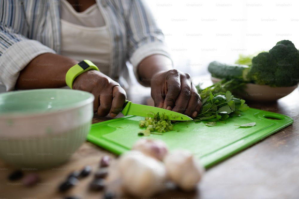 Mantener la dieta. Mujer de piel oscura usando un cuchillo de colores mientras prepara ensalada para la cena