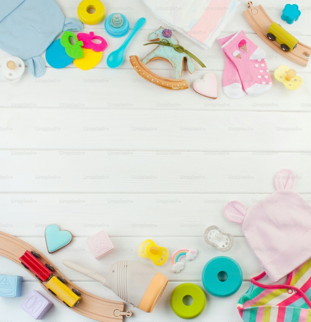 Vêtements, jouets et accessoires pour bébés sur fond en bois blanc avec espace vide pour le texte ; vue de dessus, pose à plat