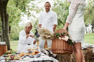 Three friends near the table with food outdoors. Girl holds basket with dry plants.