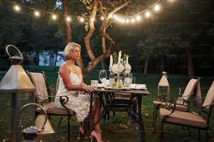 Adult woman sits on the chair with candles and wine glasses in the outdoor part of restaurant.