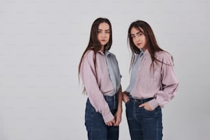 Two sisters twins standing and posing in the studio with white background.