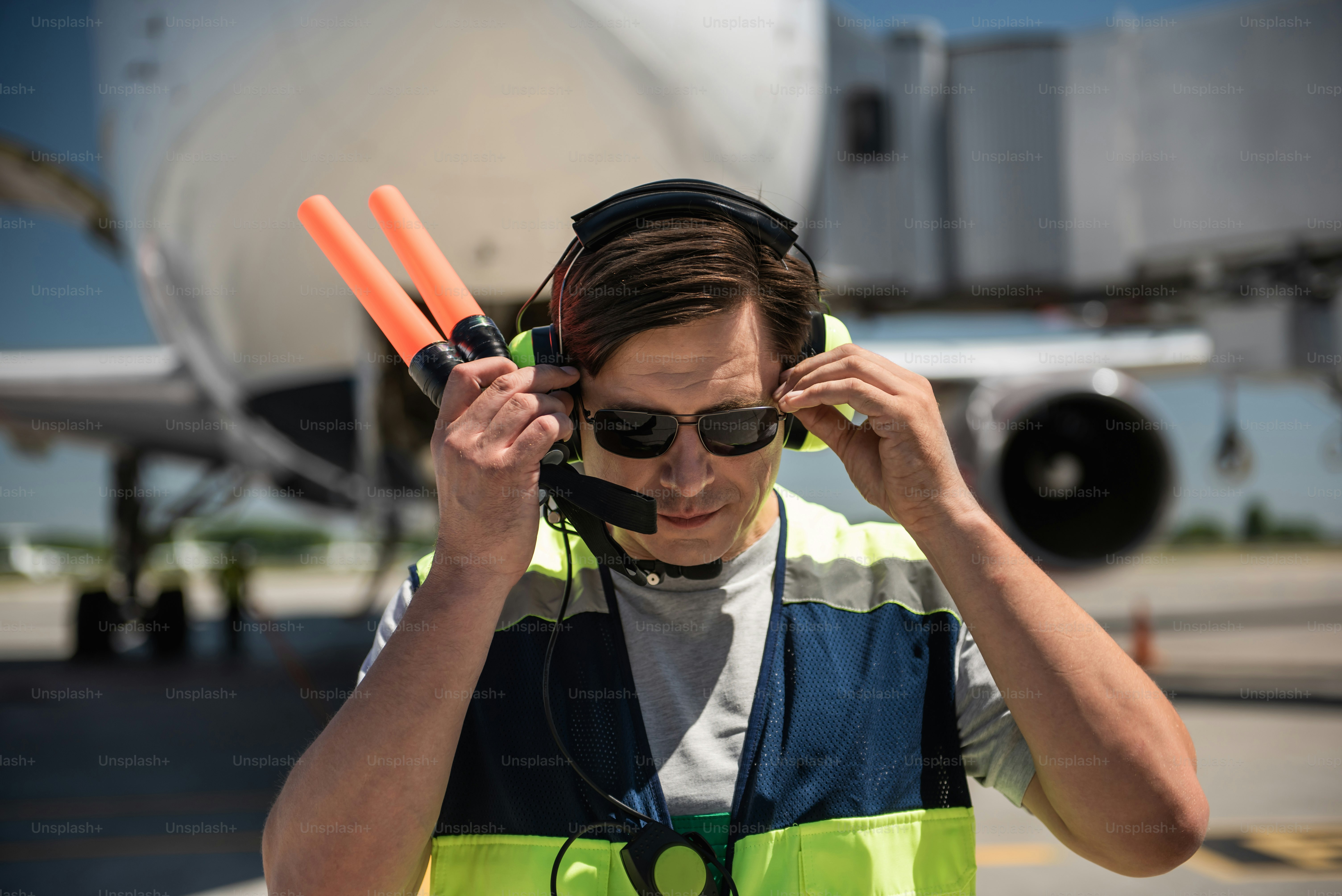 Seeing something interesting. Airport worker putting shades on and looking down. Passenger plane on blurred background