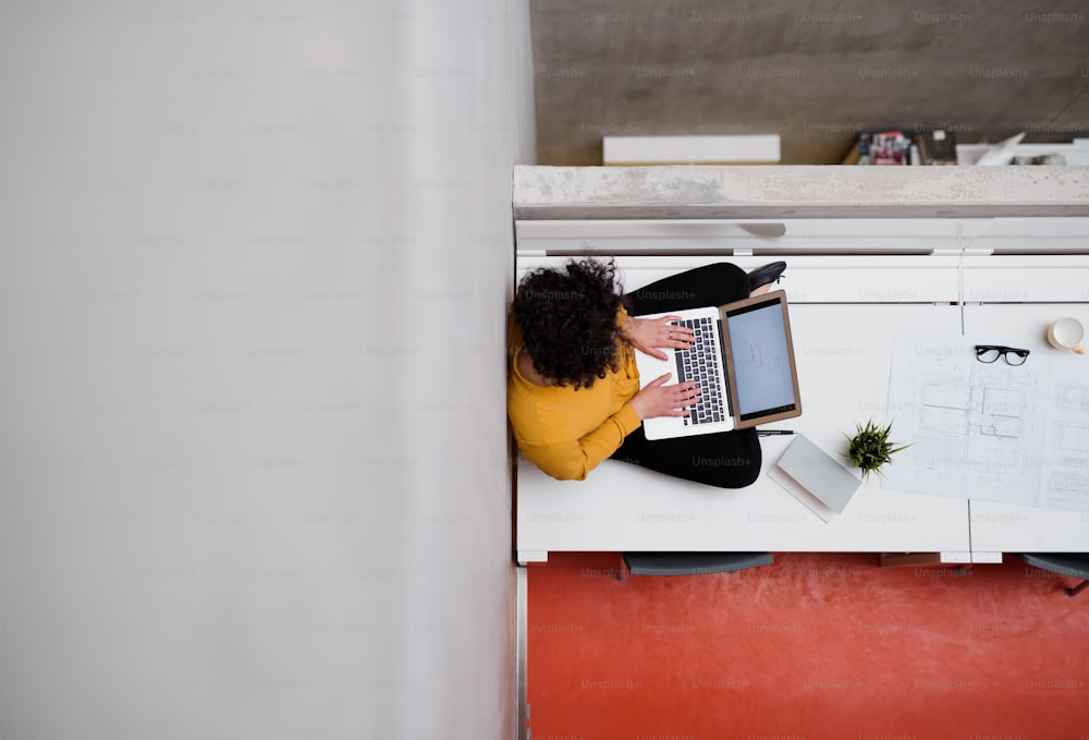 Uma visão superior de uma jovem empresária ou arquiteta sentada na mesa de um escritório, usando laptop. Espaço de cópia.