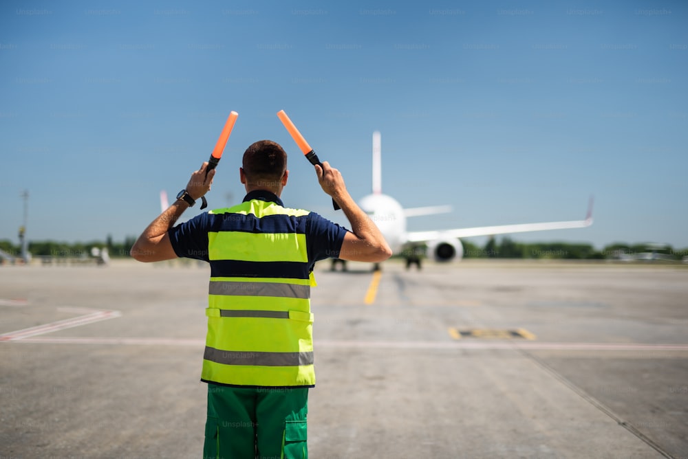 Directing the jet. Back view of aviation marshaller at airport. Aircraft, runway and sky on blurred background